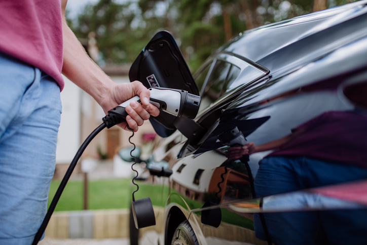 A man holding power supply cable at electric vehicle charging station, closeup