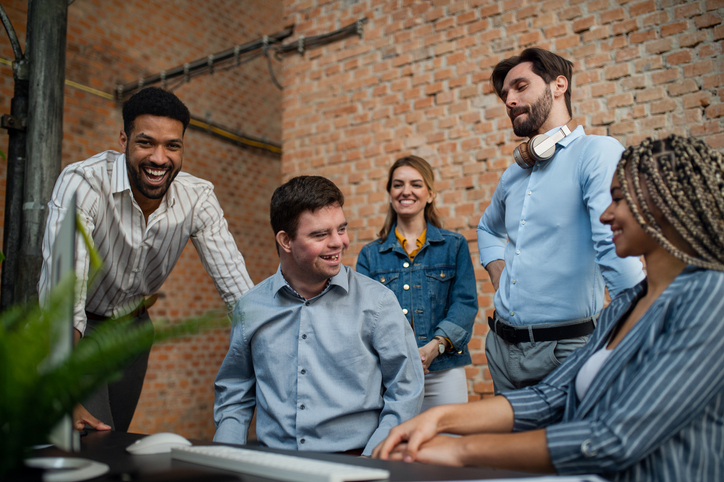 A happy down syndrome man with business colleagues in office, social inclusion and cooperation concept.